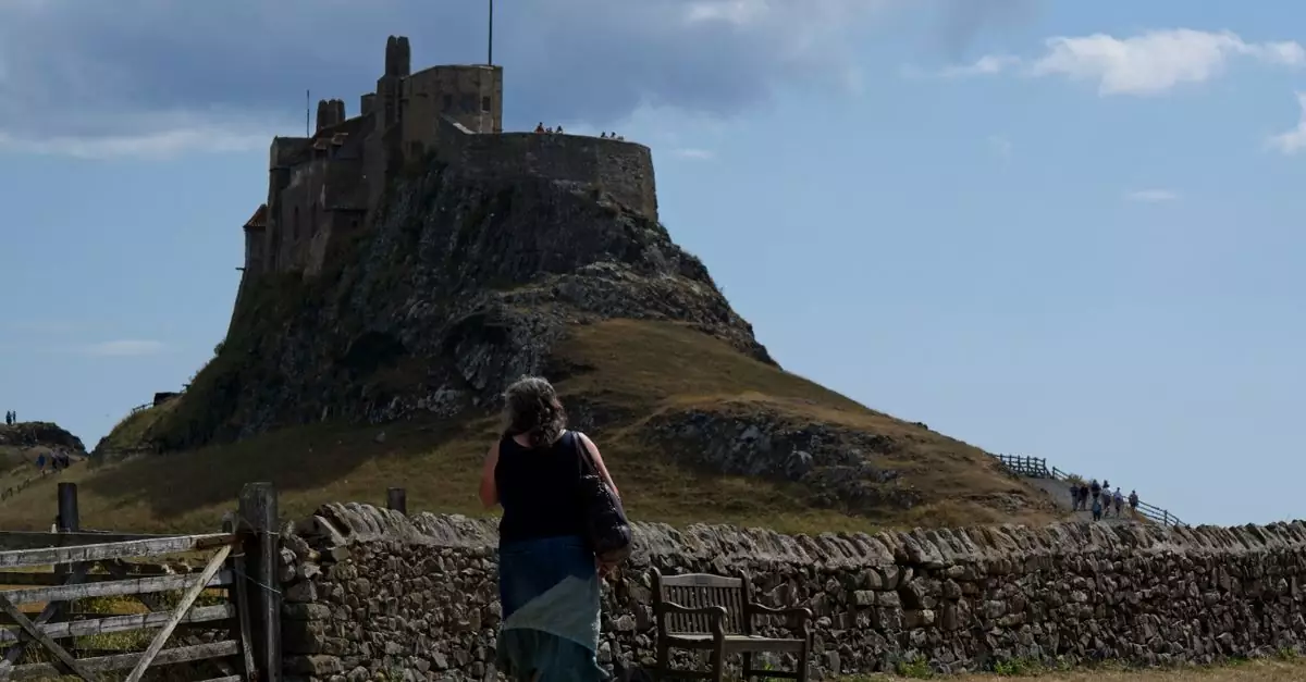 A woman walks towards the historic Lindisfarne Castle on a sunny day in Northumberland, UK.
