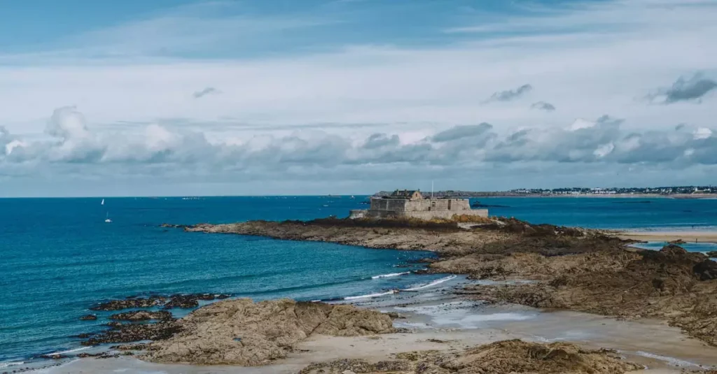 Breathtaking view of a historic fortress on the rocky coastline of Saint-Malo, France under a vibrant blue sky.