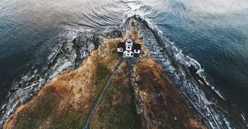 A scenic aerial view of a lighthouse perched on a rocky coastline surrounded by ocean waves.