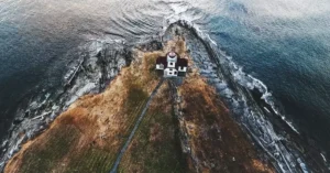 A scenic aerial view of a lighthouse perched on a rocky coastline surrounded by ocean waves.