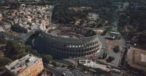 High angle drone shot of the Colosseum in Rome, Italy, showcasing its grandeur and surrounding urban landscape.