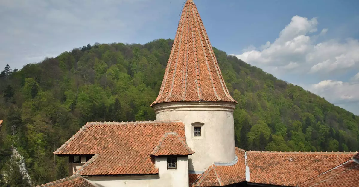 Tower of historic Bran Castle with lush green hills behind under a partly cloudy sky.