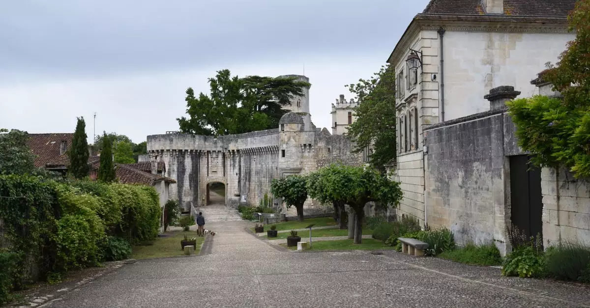 Scenic view of a rustic stone fortress entrance in a quaint French village, surrounded by lush greenery.