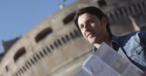 Man in denim jacket sightseeing near historical building, enjoying travel with map.